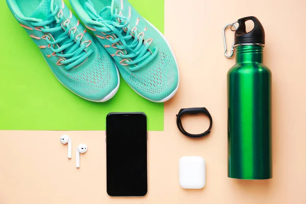 Sports water bottle, shoes, mobile phone and gadgets on color background — Stock Photo, Image