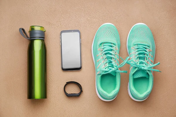 Sports water bottle, shoes, mobile phone and fitness tracker on color background