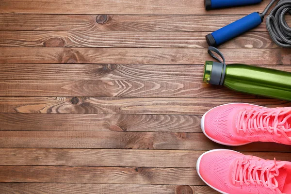 Sports water bottle, shoes and jumping rope on wooden background