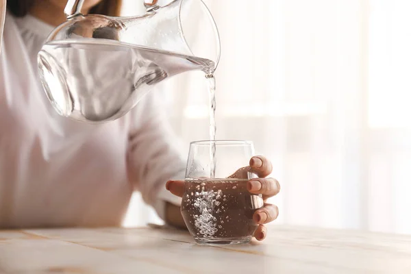 Žena nalévá sladkou vodu z džbánu do skla na stůl — Stock fotografie