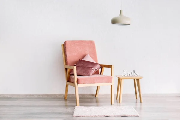 Stylish armchair with table and lamp near white wall — Stock Photo, Image