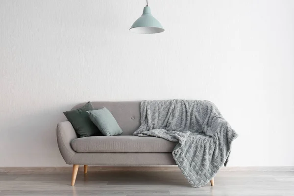Stylowa sofa z lampą w pobliżu białej ściany — Zdjęcie stockowe