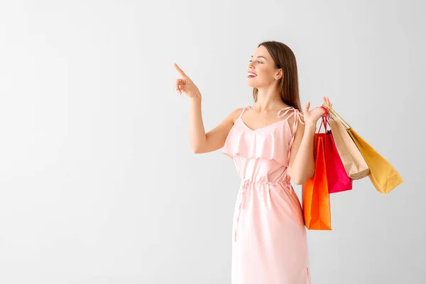 Mulher bonita com sacos de compras apontando para algo no fundo claro — Fotografia de Stock