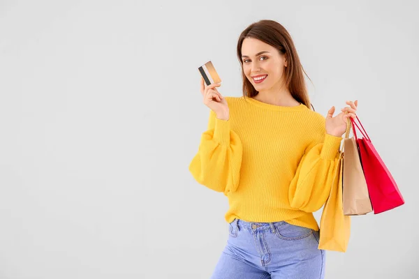 Hermosa mujer joven con bolsas de compras y tarjeta de crédito sobre fondo claro —  Fotos de Stock