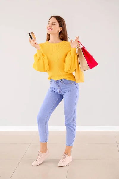 Belle jeune femme avec des sacs à provisions et carte de crédit près du mur léger — Photo