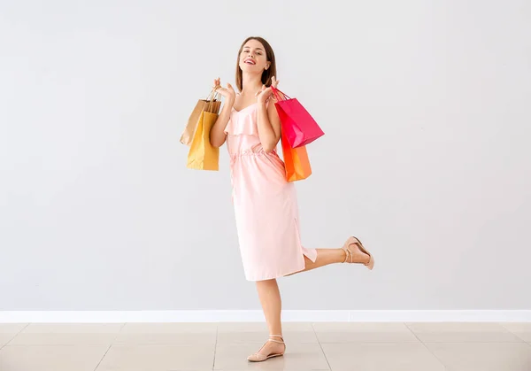 Mulher bonita com sacos de compras perto da parede de luz — Fotografia de Stock