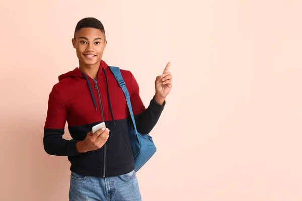 Portrait of African-American teenage boy with mobile phone pointing at something on color background — Stock Photo, Image