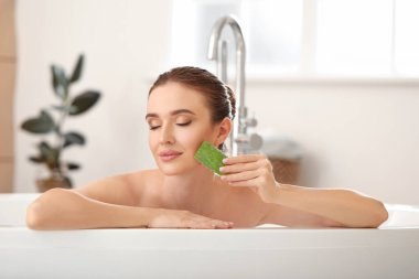 Güzel genç bir kadın banyoda aloe vera kullanıyor.