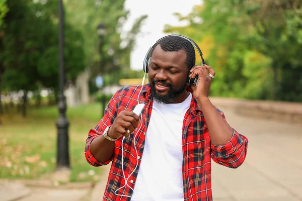 Handsome African-American man listening to music and using phone as imaginary microphone outdoors — Stock Photo, Image