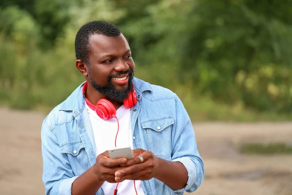 Handsome African-American man with mobile phone and headphones outdoors — Stock Photo, Image