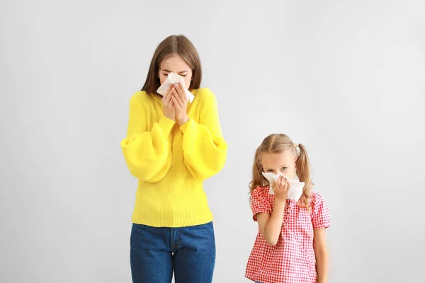 Mujer joven y niña que sufre de alergia en un fondo claro — Foto de Stock