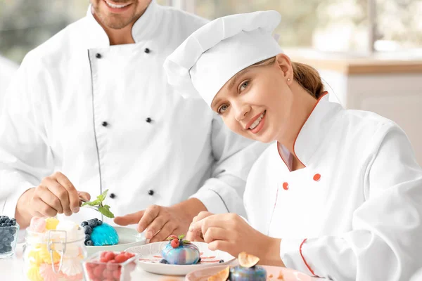 Jeunes confiseurs décorant le dessert savoureux dans la cuisine — Photo