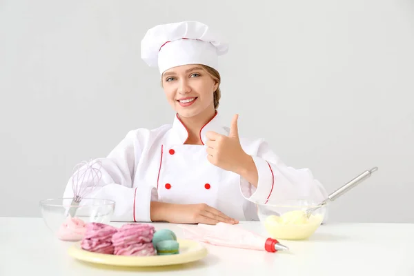 Dolcificante femminile con gustosi dessert che mostrano un gesto pollice su sfondo chiaro — Foto Stock