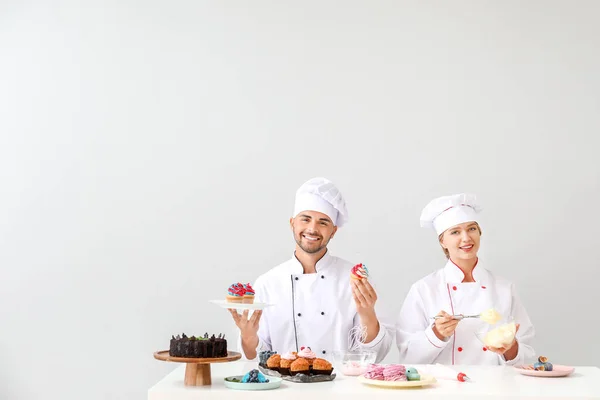 Jóvenes pasteleros cocinando sabrosos postres sobre fondo claro —  Fotos de Stock