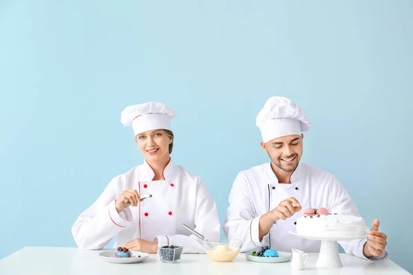 Jóvenes pasteleros cocinando sabrosos postres sobre fondo de color — Foto de Stock