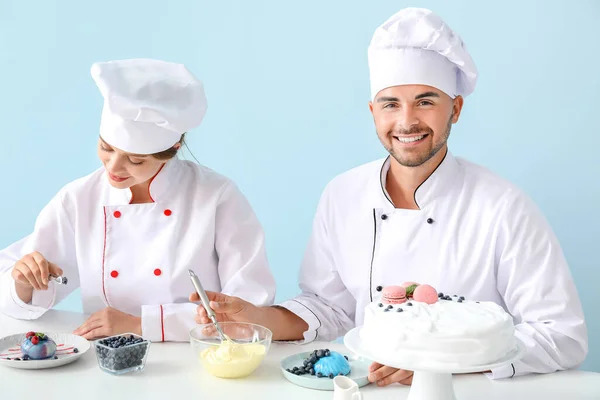 Young confectioners cooking tasty desserts against color background — Stock Photo, Image