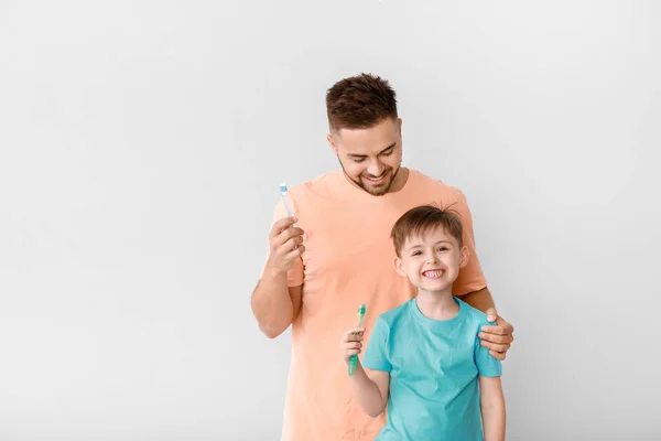 Portrait of man and his little son brushing teeth on light background — Stock Photo, Image