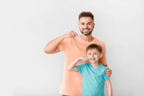 Portrait of man and his little son brushing teeth on light background — Stock Photo, Image