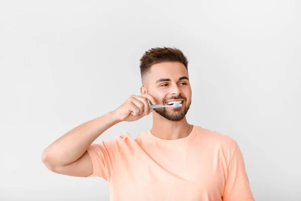 Portret van de mens poetsen tanden op lichte achtergrond — Stockfoto