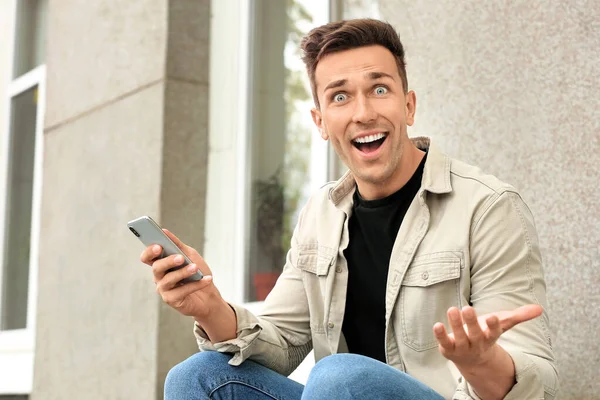 Έκπληκτος νεαρός άνδρας με κινητό τηλέφωνο έξω — Φωτογραφία Αρχείου