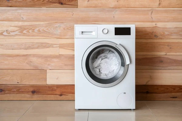 Mesin cuci modern dengan cucian dekat dinding kayu — Stok Foto