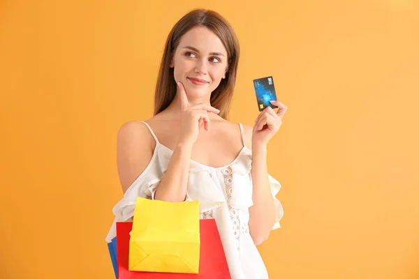 Átgondolt fiatal nő bevásárló táskák és hitelkártya színes háttér — Stock Fotó