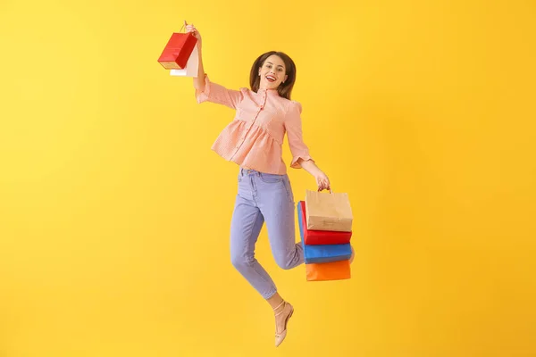 Feliz salto mujer joven con bolsas de compras en el fondo de color —  Fotos de Stock