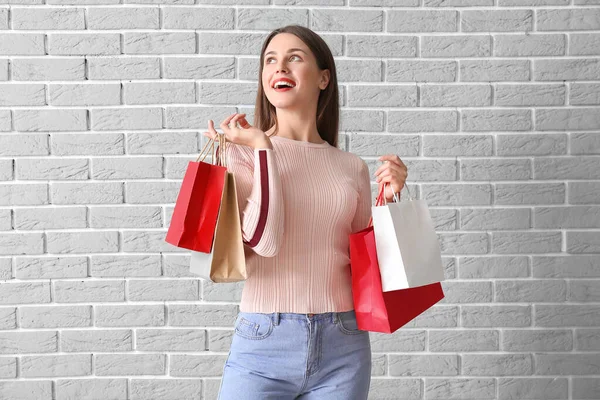 Belle jeune femme avec des sacs à provisions sur fond de brique — Photo