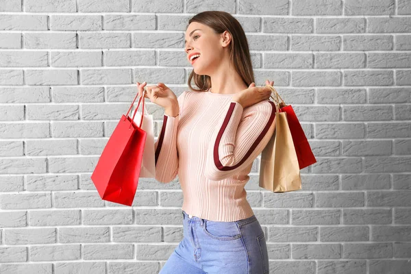 Beautiful young woman with shopping bags on brick background — Stock Photo, Image