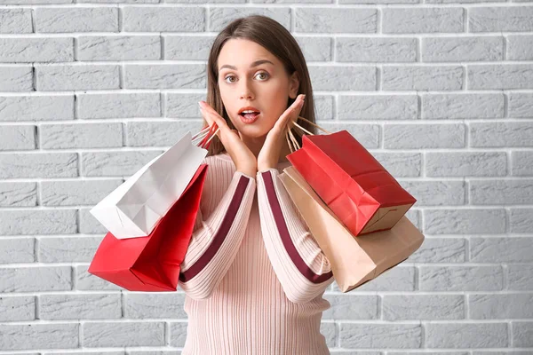 Surpreendida jovem mulher com sacos de compras no fundo de tijolo — Fotografia de Stock