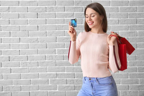 Mooie jonge vrouw met boodschappentassen en creditcard op bakstenen achtergrond — Stockfoto