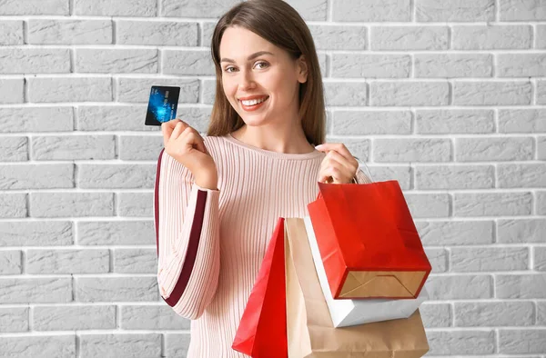 Beautiful young woman with shopping bags and credit card on brick background — Stock Photo, Image