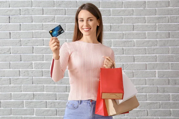Krásná mladá žena s nákupními taškami a kreditní karty na cihlovém pozadí — Stock fotografie