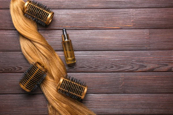 Hair strand, curlers and oil on wooden background — Stock Photo, Image