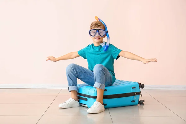 Cute little boy with snorkeling mask sitting on suitcase near color wall — Stock Photo, Image