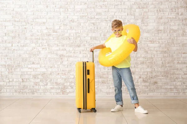 Cute little boy with suitcase and swimming ring near brick wall — Stock Photo, Image