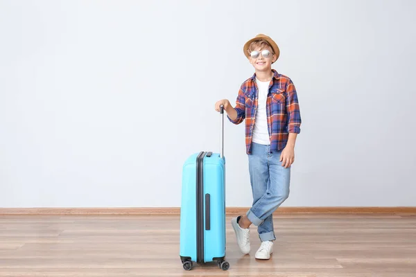 Netter kleiner Junge mit Koffer in der Nähe von Lichtwand — Stockfoto