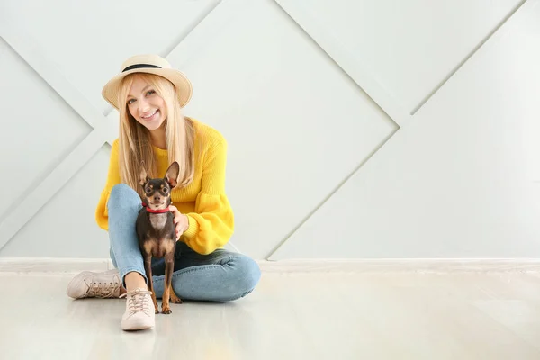 Красивая молодая женщина с милой игрушечной собакой-терьером сидит напротив светлой стены — стоковое фото