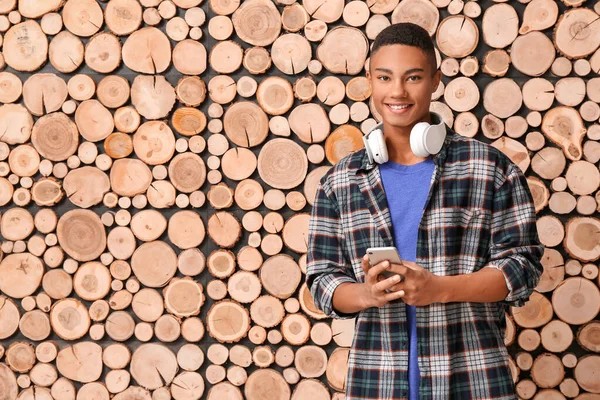 Menino adolescente afro-americano com fones de ouvido e telefone celular em fundo de madeira — Fotografia de Stock