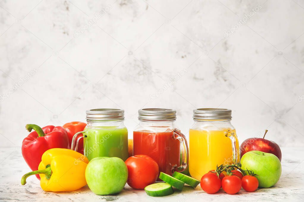 Mason jars of fresh juices with ingredients on light background