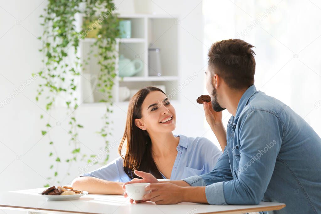 Happy young couple drinking coffee with cookies in kitchen at home