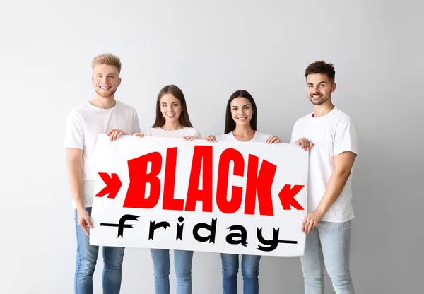 Group of young people holding poster with inscription BLACK FRIDAY on light background — Stock Photo, Image