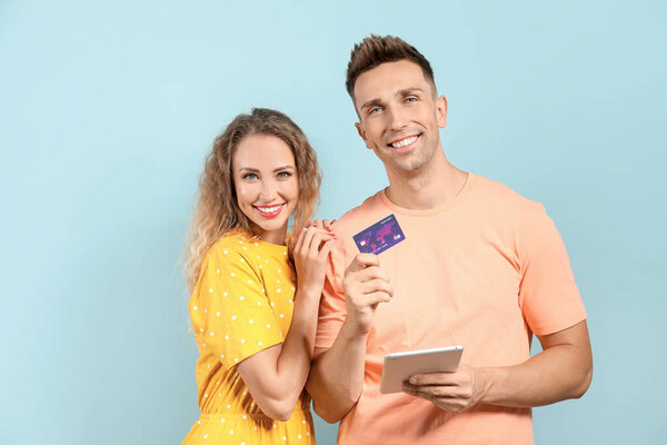 Young couple with credit card and tablet computer on color background