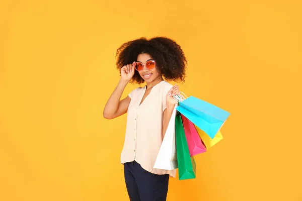 Bella donna afro-americana con borse della spesa su sfondo colore — Foto Stock