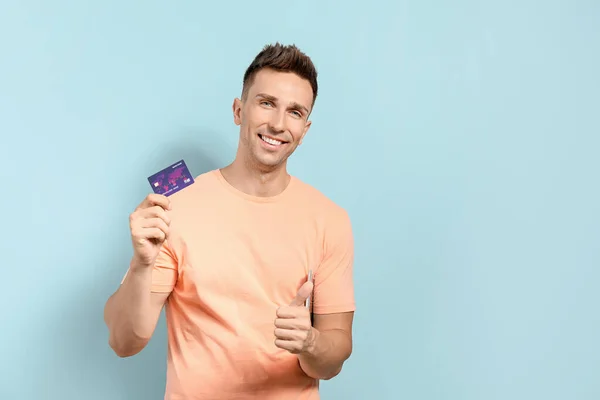 Mladý muž s kreditní kartou ukazující palec nahoru gesto na barevném pozadí — Stock fotografie