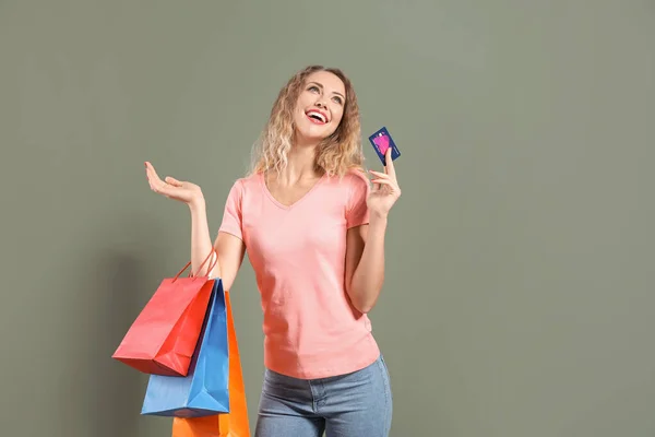 Jonge vrouw met credit card en boodschappentassen op kleur achtergrond — Stockfoto