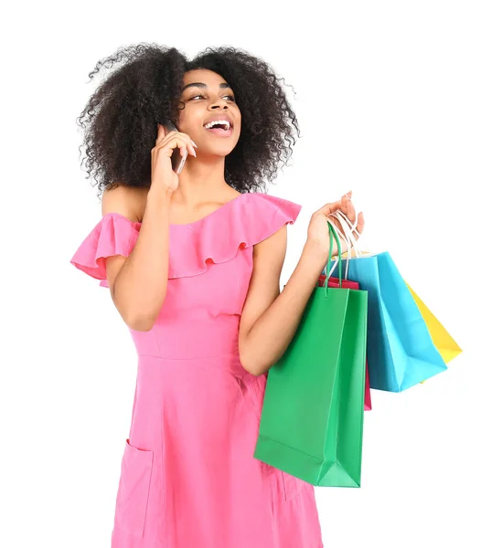 Beautiful African-American woman with shopping bags talking by phone on white background — Stock Photo, Image