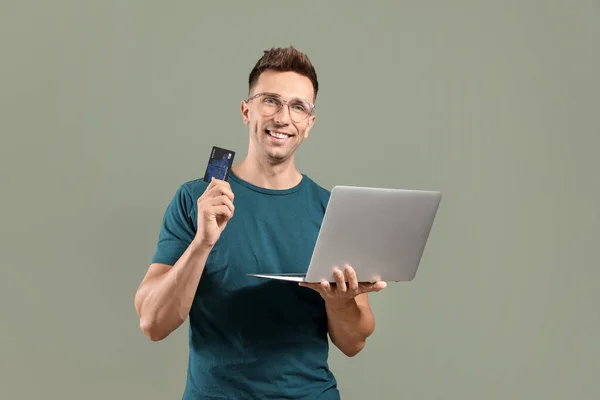 Молодий чоловік з кредитною карткою та ноутбуком на кольоровому фоні — стокове фото