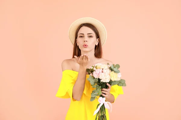 Beautiful young woman with bouquet of carnation flowers blowing kiss against color background — Stock Photo, Image