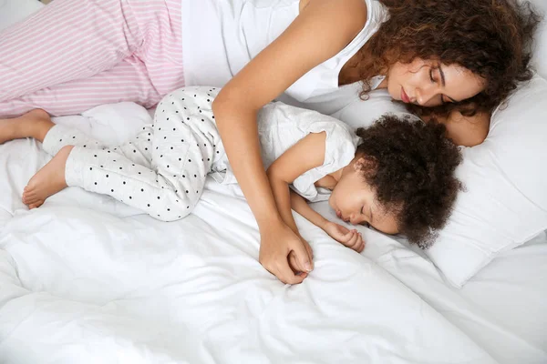 Liten afro-amerikansk flicka med mamma sover i sängen — Stockfoto